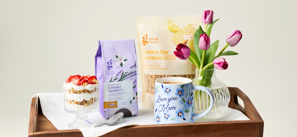 A wooden tray is holding a bag of Good & Gather coffee, Good & Gather granola, a vase filled with purple tulips, and yogurt, granola and strawberries in a glass bowl.