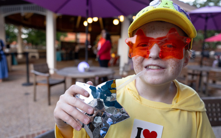 A child smiles wearing sunglasses and holding a silver star.