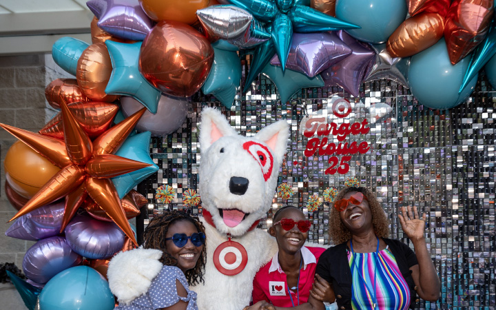 Three people pose with Bullseye in front of balloons and a banner reading "Target House 25."