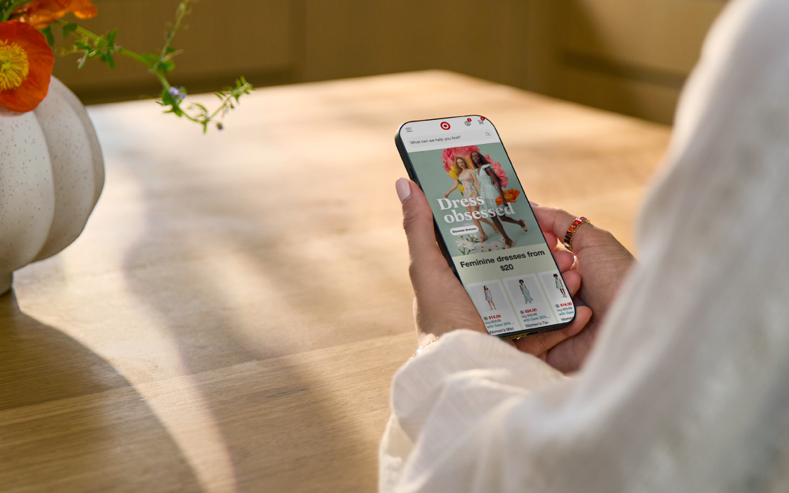 A person holds a smartphone displaying the Target app with spring fashion featured on the screen.